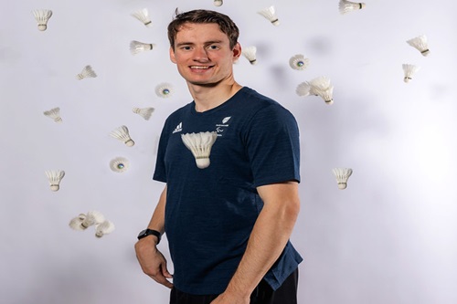 Dan smiling at camera in front of a blank screen surrounded by shuttlecocks flying through the air